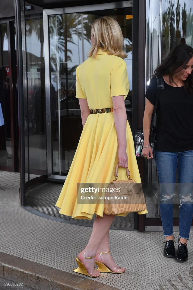 Kirsten Dunst walking in a yellow dress and heels outside a building.