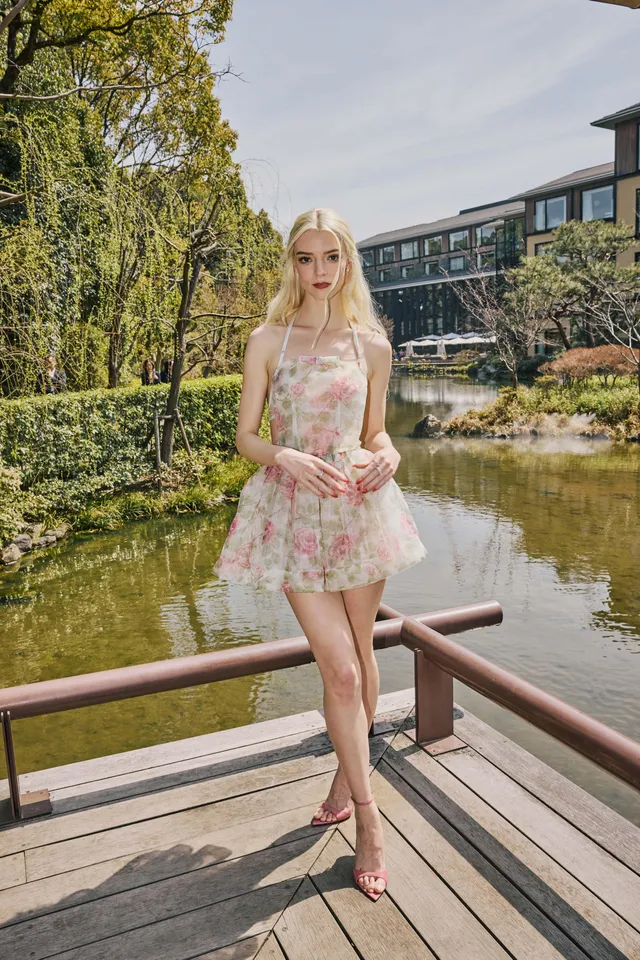 Anya Taylor-Joy standing barefoot on a wooden balcony in a floral outfit.
