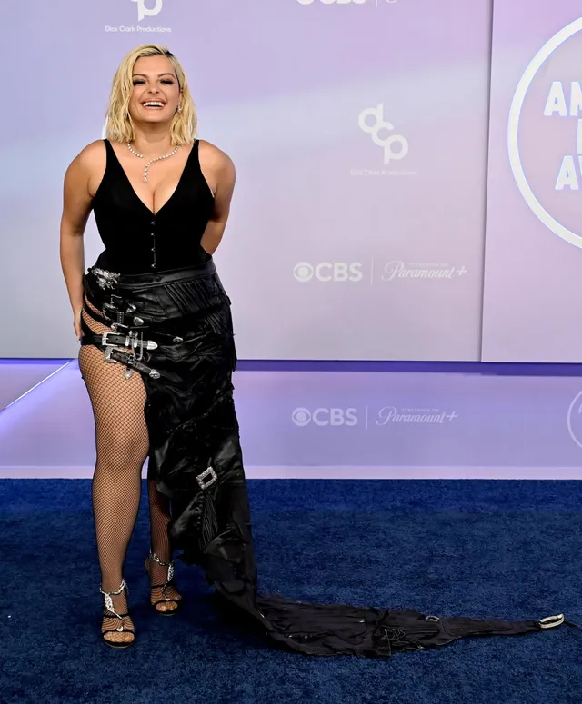 Bebe Rexha posing at an event in a black gown and metallic heels.