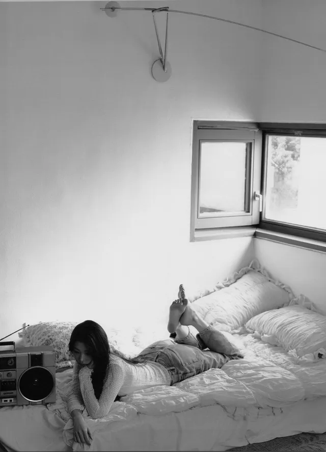 Jang Wonyoung lying on a bed with bare feet raised in a monochrome photograph.