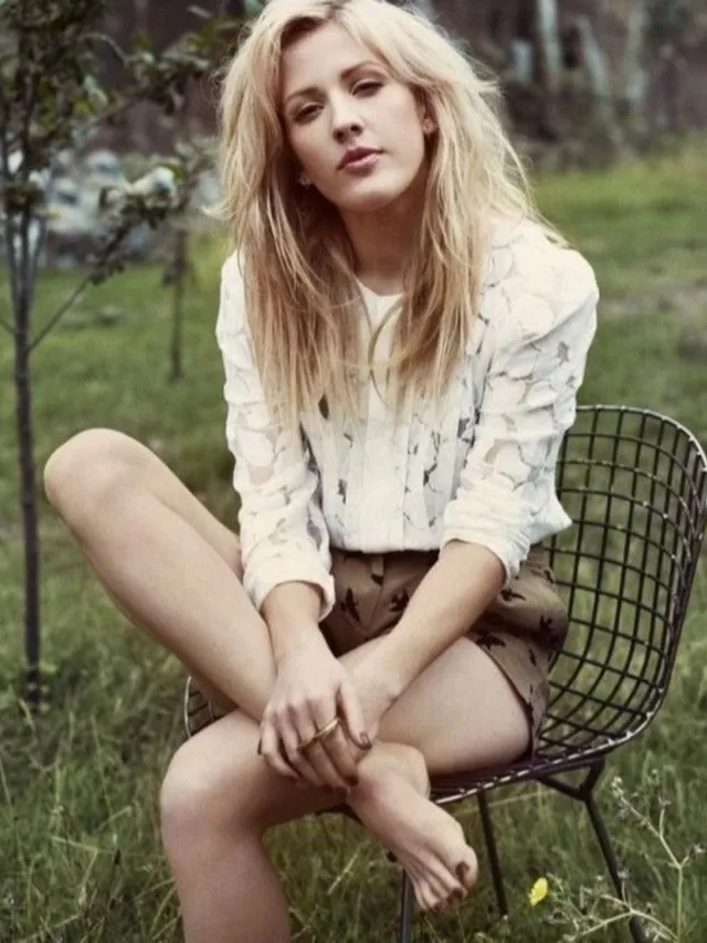 Ellie Goulding sitting barefoot in an outdoor wire chair.