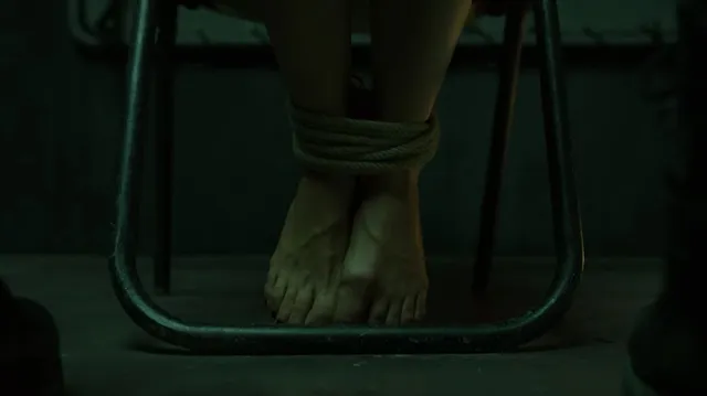 Úrsula Corberó shown with bare feet beside a chair in a film scene.