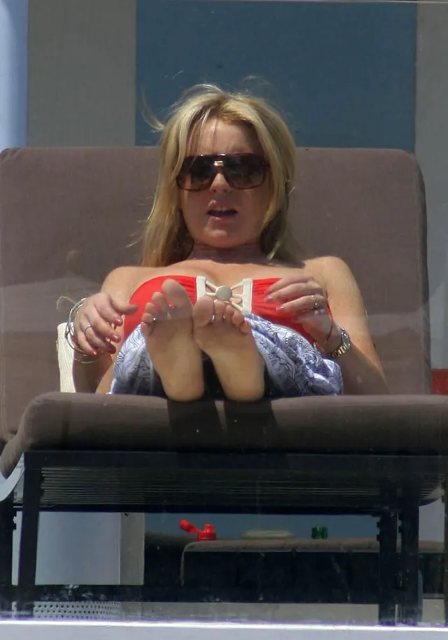 Lindsay Lohan reclining barefoot on a sun lounger in a red top.
