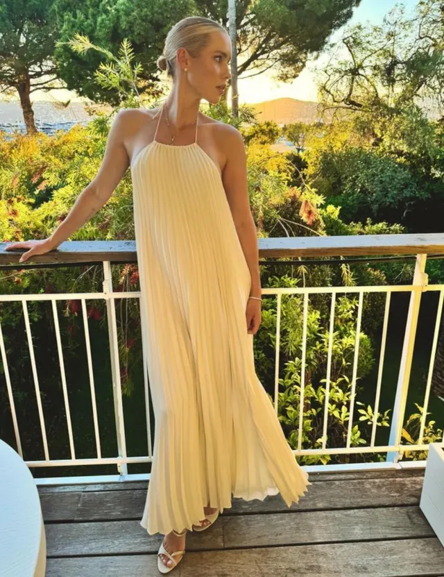 Claire Holt standing on a balcony in a long yellow dress.