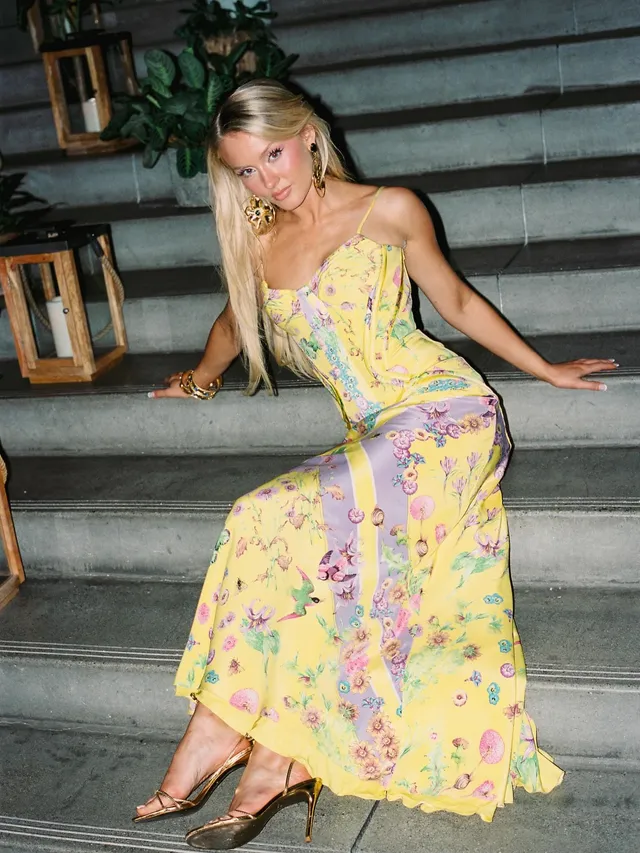 Zara Larsson sitting on stairs wearing a yellow dress and gold heels.