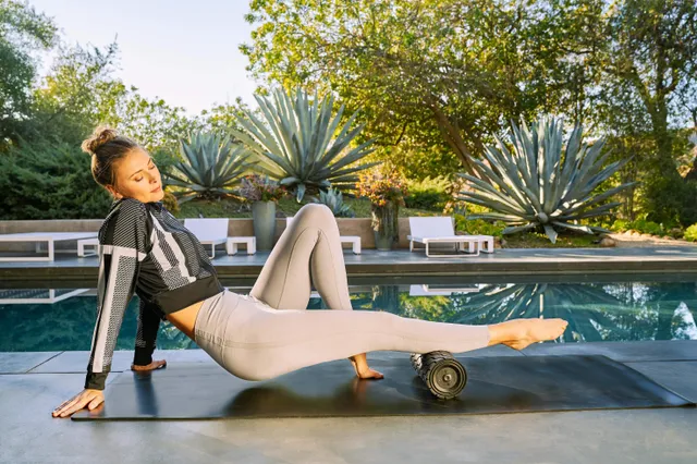 Maria Sharapova stretching barefoot on an outdoor mat with a foam roller.