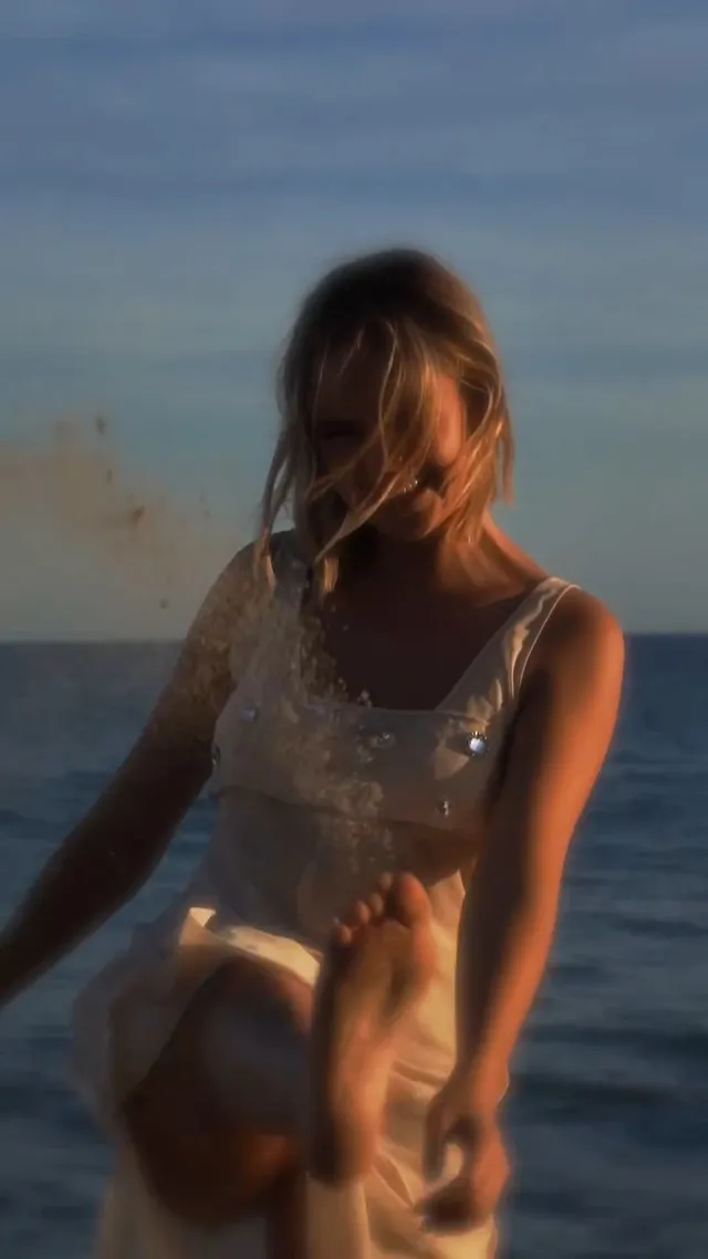 Bailee Madison sitting beside the sea with a bare foot raised.