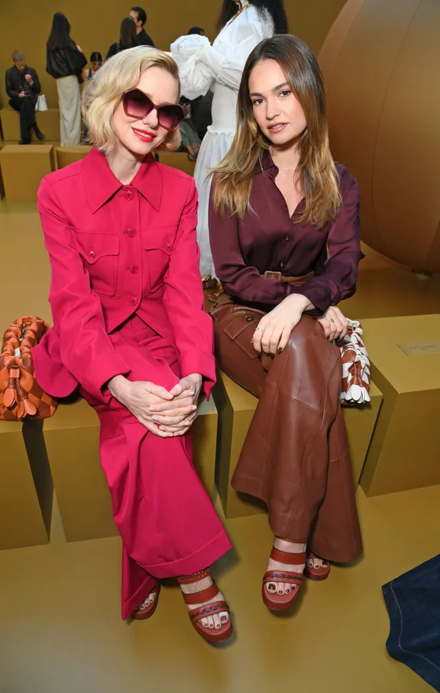 Lily James sitting beside another guest in brown trousers and heels.