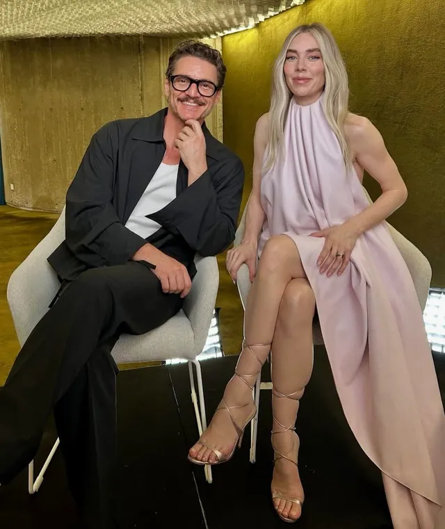 Vanessa Kirby seated beside a companion in a pale dress and heels.