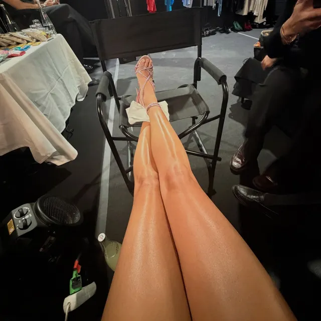 Dua Lipa: bare legs and feet extended beside a chair.