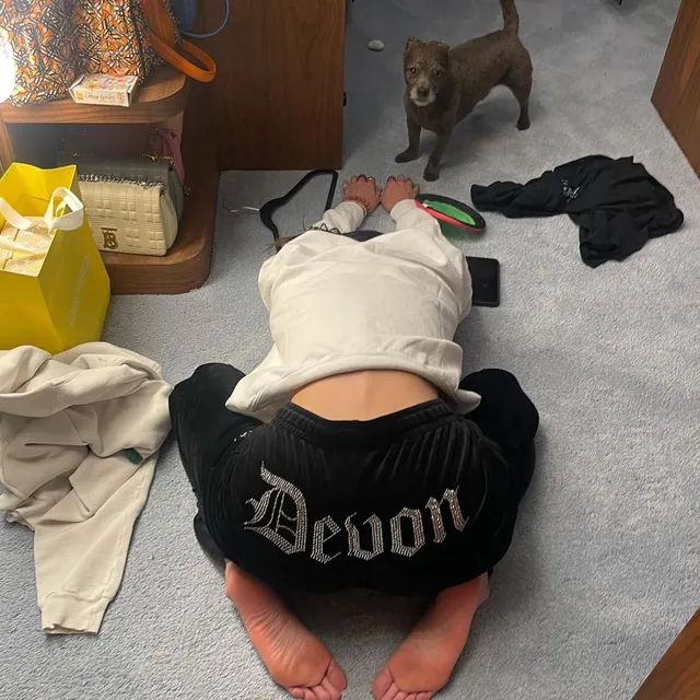 Bella Hadid kneeling barefoot in a dark skirt beside a dog.