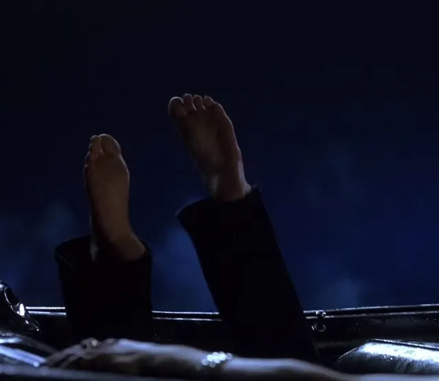 Anne Hathaway raising bare soles in a dark screen scene.