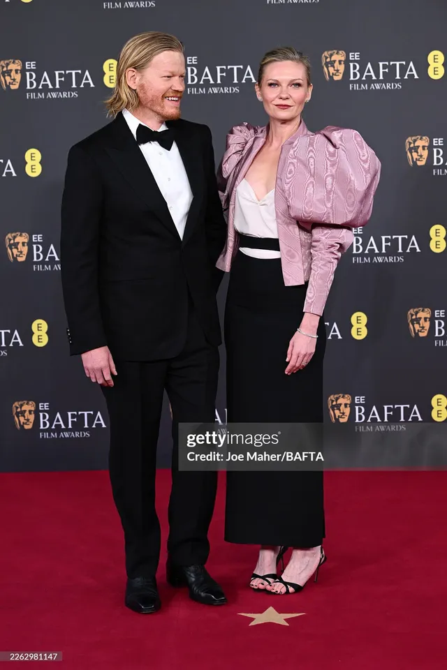Kirsten Dunst posing in a pink jacket and black skirt at an awards event.