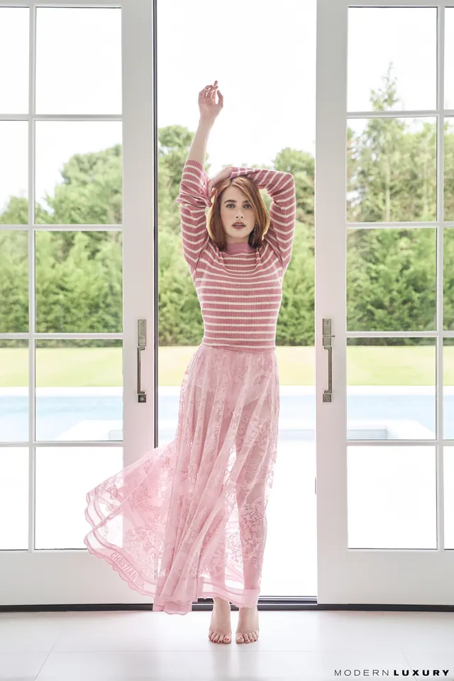 Emma Roberts posing in a striped top and pink skirt with heels.