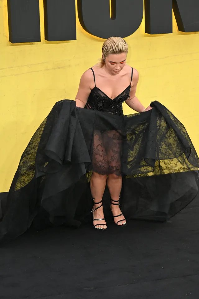 Florence Pugh sitting in a layered black dress and strappy heels.