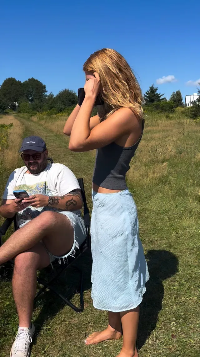 Sophie Nélisse standing barefoot on grass beside a seated man.