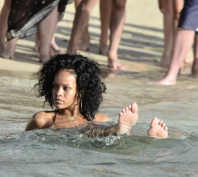Rihanna floating in the sea with both bare soles above the water.