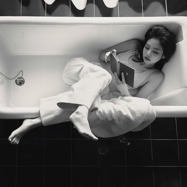 Jennie Kim reclining barefoot beside a bath in a monochrome photograph.