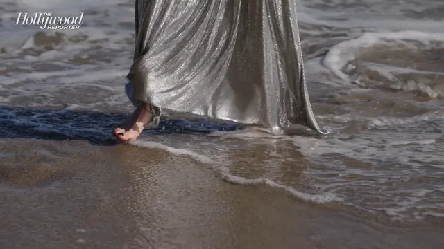 Anya Taylor-Joy a close view of her bare foot at the water's edge beneath a silver dress.