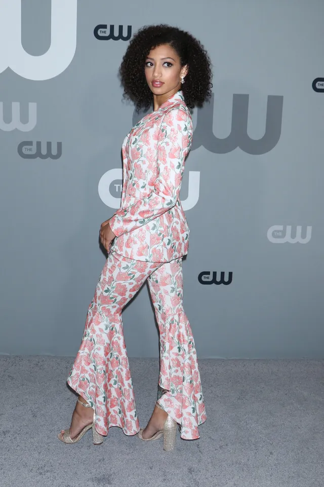 Samantha Logan posing sideways in a floral trouser suit and gold heels.