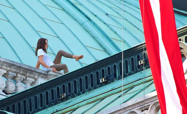 Rebecca Ferguson sitting barefoot on a rooftop railing during a film scene.