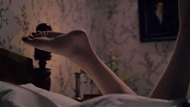 Hailee Steinfeld raising bare feet in a candlelit bedroom scene.