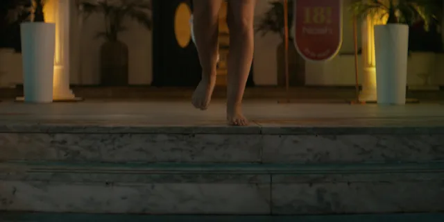 Nicole Wallace shown standing barefoot on an outdoor deck in a scene.