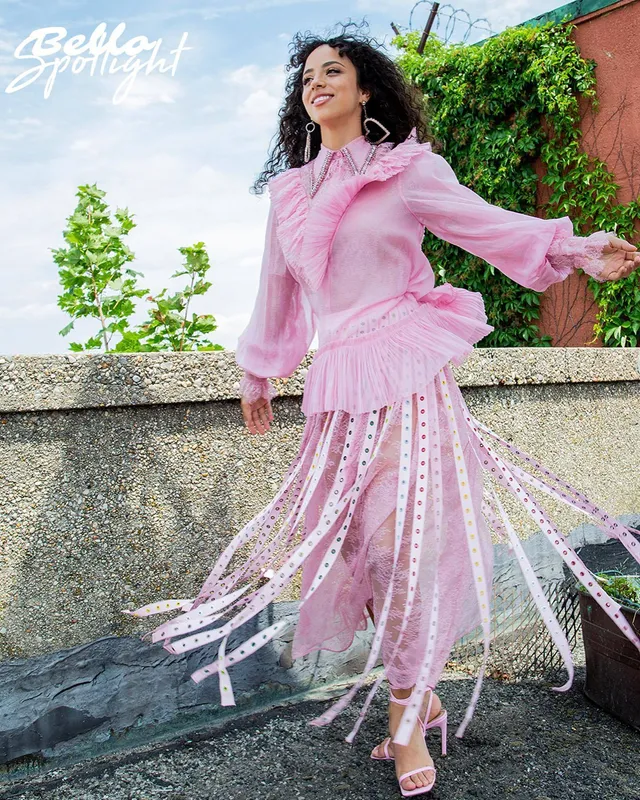 Kiana Madeira posing outdoors in a flowing pink outfit and white heels.