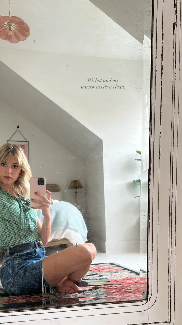 Daisy Edgar-Jones posing for a mirror photograph in a blouse and denim skirt.