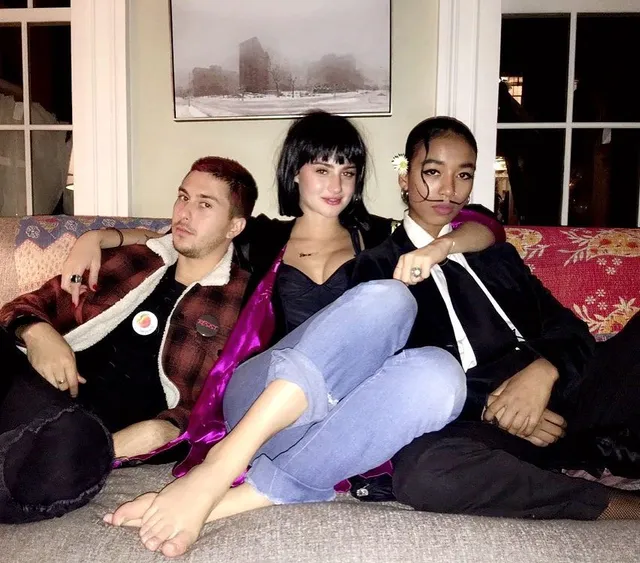 Grace Van Patten sitting barefoot between two people on a sofa.