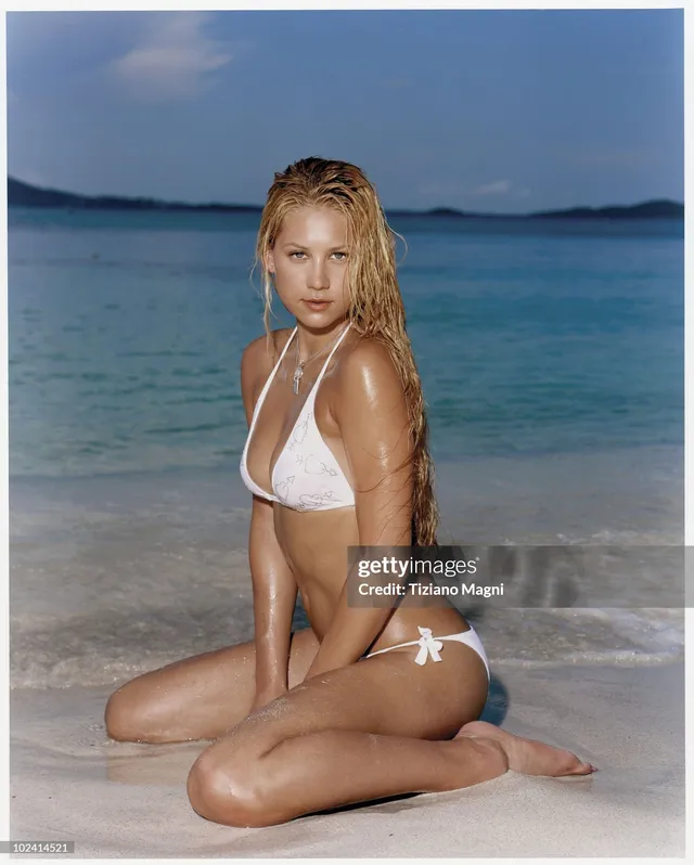 Anna Kournikova kneeling barefoot on wet sand in white swimwear.