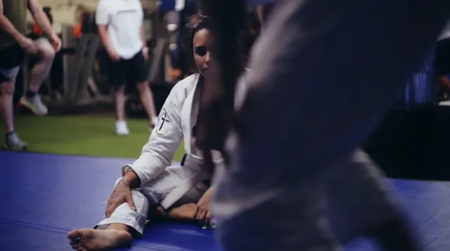 Demi Lovato sitting barefoot on a floor in a video scene.