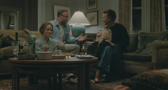 Olivia Wilde sitting with other people around a table in a film scene.