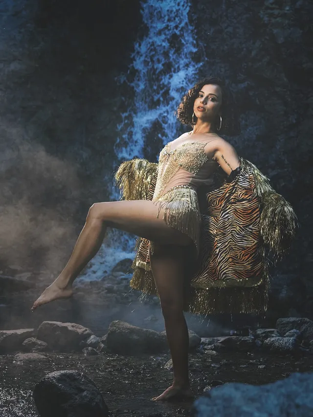 Kiana Madeira posing barefoot on rocks beside a waterfall in a patterned outfit.