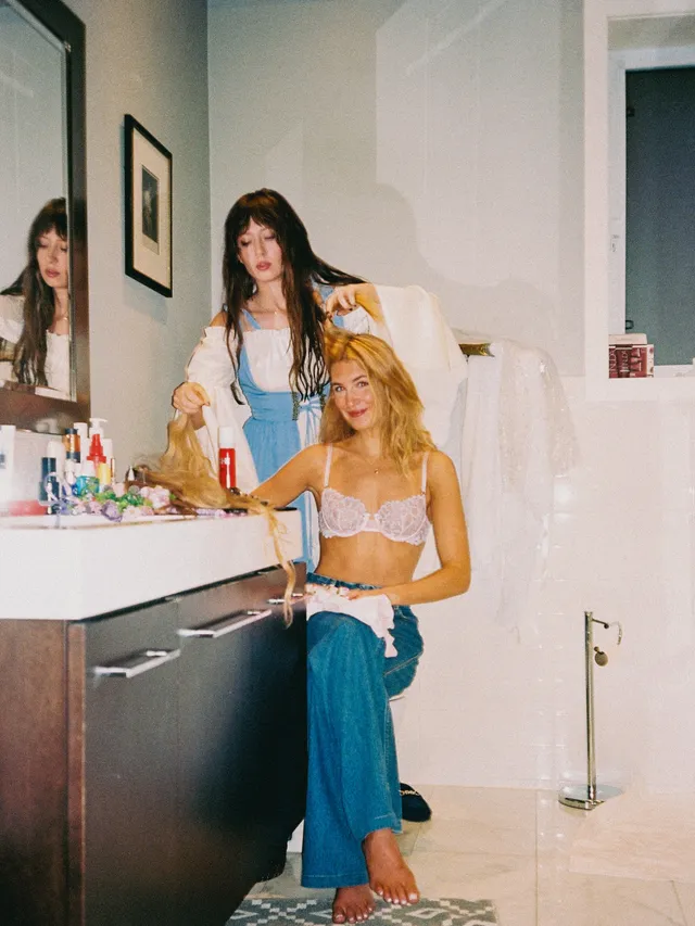 Sophie Nélisse sitting barefoot at a dressing table beside another woman.