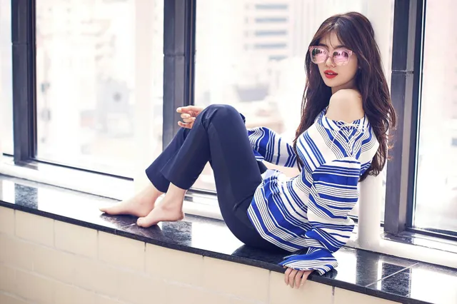 Bae Suzy sitting barefoot beside a window.