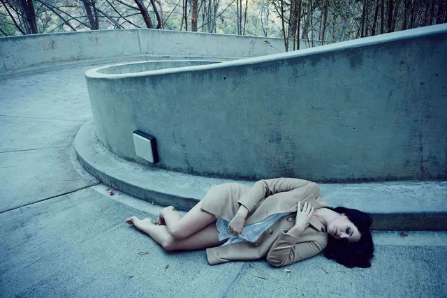 Lana Del Rey lying beside a curved wall in high heels.