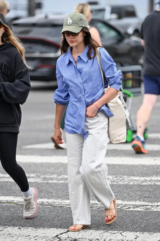 Lucy Hale crossing a street in a cap and flip-flops.