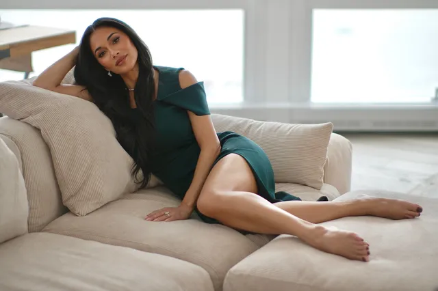 Nicole Scherzinger reclining barefoot on a pale sofa in a green dress.