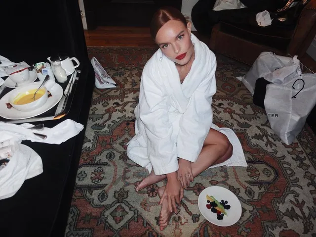 Kate Bosworth sitting in a robe on a carpet beside shoes.