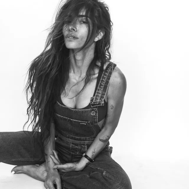 Sarah Shahi sitting for a black-and-white portrait in overalls.