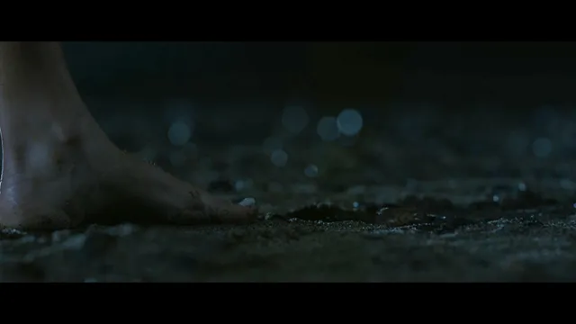 Emily Alyn Lind shown stepping barefoot on a dark outdoor surface.