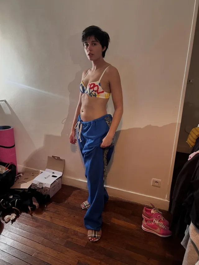 Naomi Scott posing in blue trousers and heels indoors.