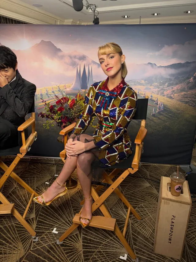 Mckenna Grace sitting in a director's chair wearing gold heeled sandals.