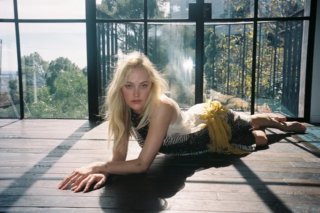 Maika Monroe lying barefoot on a wooden floor.
