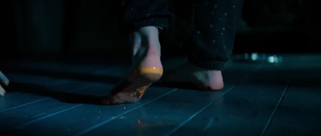 Sophie Thatcher showing a bare sole while stepping on a blue-lit floor.