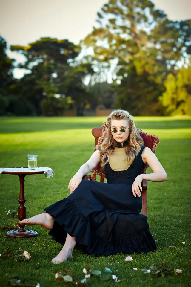 Natalie Dormer sitting in an armchair on a lawn.