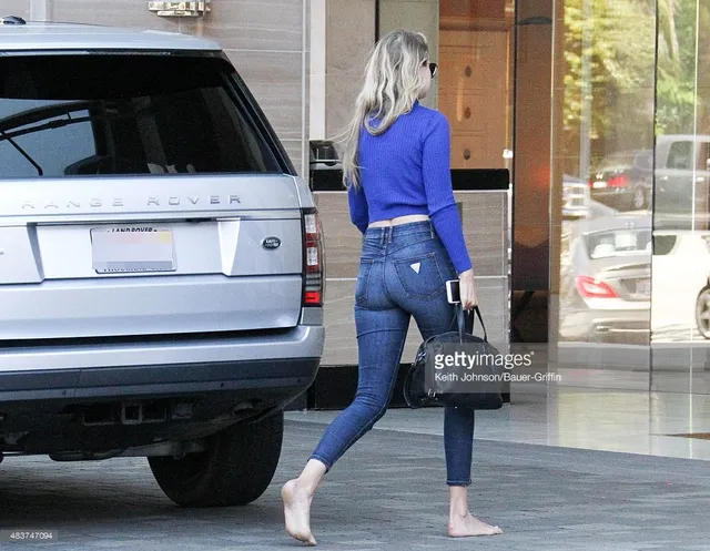 Gigi Hadid walking barefoot beside a car in jeans.