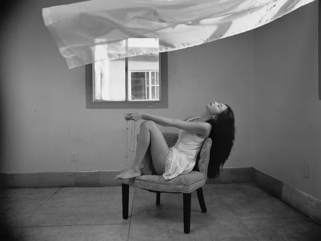 Jennie Kim sitting barefoot in a chair beneath flowing fabric during a monochrome shoot.