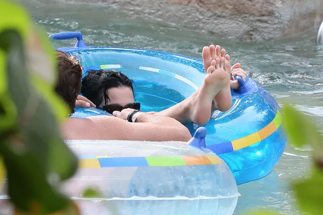 Katy Perry relaxing on an inflatable with bare soles raised.
